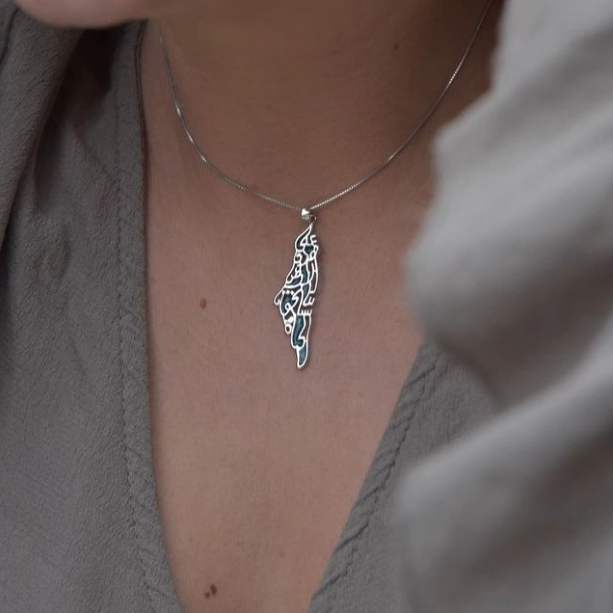 Silver Palestine map necklace with Mahmoud Darwish quote in Arabic calligraphy, handmade in Ramallah, worn.